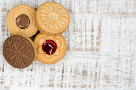 Vier runde Kekse, mit Schokolade und Marmelade, auf einem hellen Holztisch