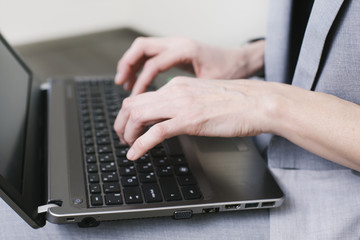 Business woman typing on the laptop on the knees with pencil in her hand in the office. Close-up hands