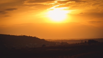 Fototapeta na wymiar Golden sun illuminates sky over the dark field and village