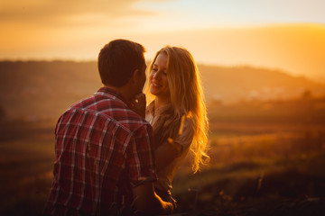 Charming couple hugs in the front of hills covered with golden s