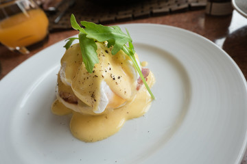 Eggs Benedict consists of an English muffin topped with ham or bacon, a poached egg and hollandaise sauce on a white plate.