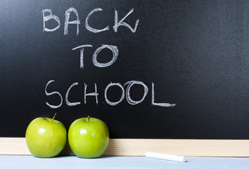Green apple in fron of blackboard with the text "back to school"