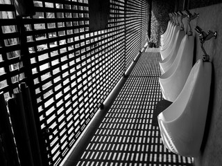 white porcelain urinal with texture of shadow at public toilet for traveler, black and white picture