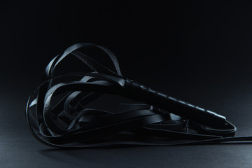 Black whip for sexual pleasure on a black background