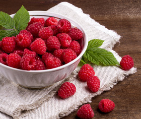 View from above on handful of ripe and fresh raspberry in white cup and some raspberry sprinkled on white wooden desk