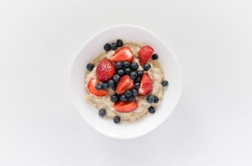 Morning oatmeal porridge with fresh strawberries and blueberries.