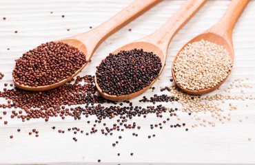 Red, black and white quinoa seeds on a wooden background