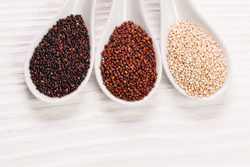 Red, black and white quinoa seeds on a wooden background