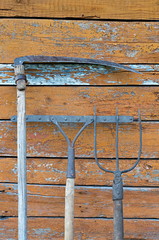 pitchfork, scythe, rake on the background of the old wooden brown wall