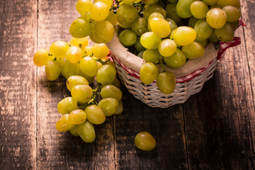 Bunch of grapes and in basket on wooden table.