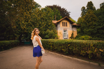 Girl in blue skirt holds her white beg while posing in the park