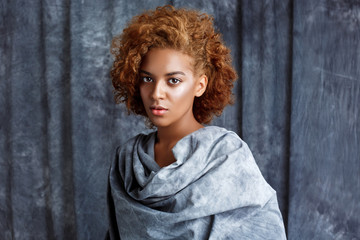 Fototapeta premium Young beautiful african girl posing, wrapping up in grey cloth.
