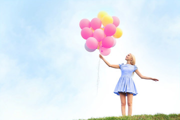 Fototapeta na wymiar Beautiful young woman holding air balloons in field