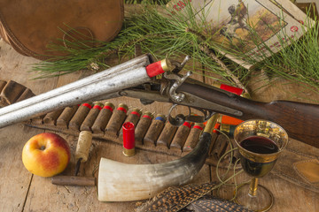 Vintage hunting gun, hunter cartridge belt, antlers, feathers, hunting horn, one glass of red wine, corkscrew, one apple and old hunter magazines    