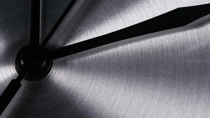 Close up of clock hands going around a stainless steel clock, with space for text