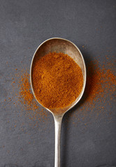 Aerial view of an old metal spoon full of chili powder spices on a rustic slate background
