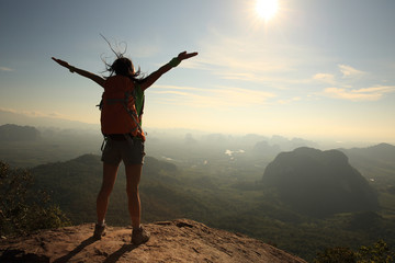 silhouette of free cheering woman hiker open arms at mountain peak