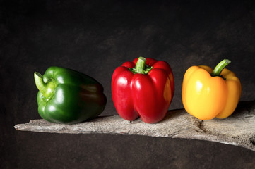 three paprika peppers in yellow, red and green on old wood with dark background