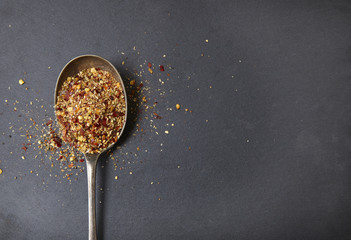 Aerial view of an old metal spoon full of peri peri seasoning, on a rustic slate background forming a page border