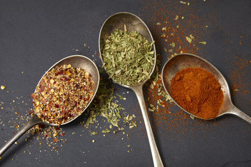 Three old silver spoons with assorted food seasonings arranged on a rustic slate background