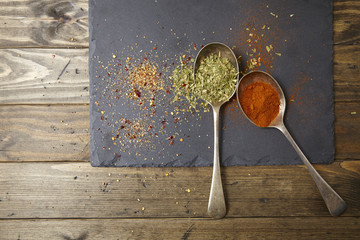 Two old silver spoons full of herbs and spices on a dark slate and wooden kitchen counter background forming a page border