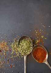 Two silver spoons full of herbs and seasoning on a dark slate background forming a page border