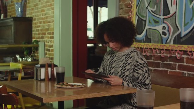 African American woman browsing on digital tablet at pizza place - 4K