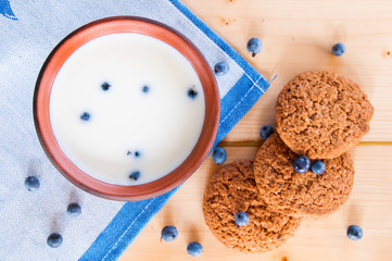 Milk in clay mug with oatmeal cookies on wooden table.