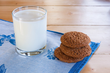 Milk in glass mug with oatmeal cookies on wooden table.