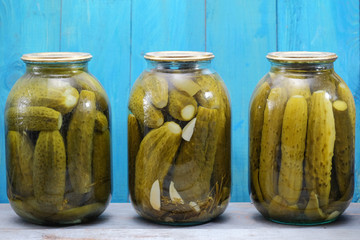 Three jars of pickled cucumbers on the wooden background