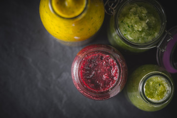 Bottles and jar with different smoothie on the dark stone table top view