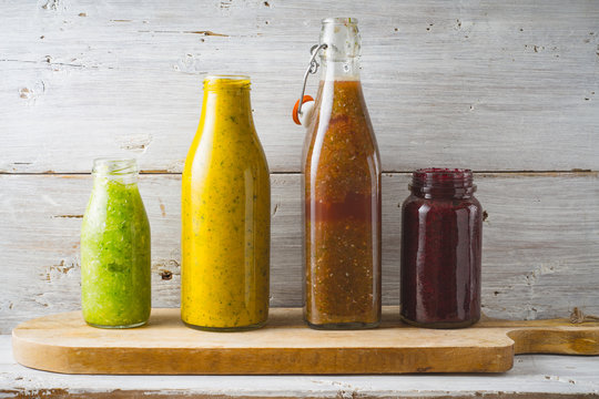 Bottles and jar with different smoothie on the white wooden background