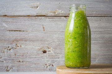Green smoothie in the glass bottle on the white wooden background