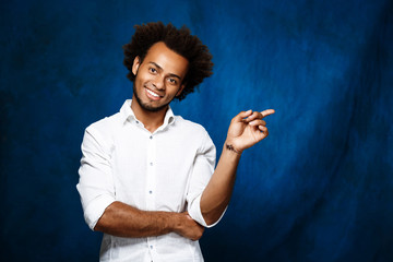 Young african man pointing finger in side over blue background.