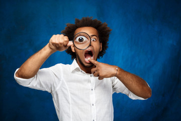 Young handsome african man posing with magnifier over blue background.