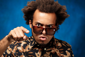 Young handsome african man in sunglasses fooling over blue background.