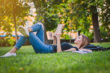 girl student in a park lying on the grass and reading a book, ly