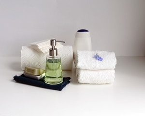 Part of a spa interior. Paper and cotton napkins, tissue, towels, soap and cosmetic products on a wooden table. White background and table, toned image. copy space