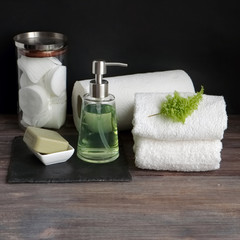 Part of a spa interior. Paper and cotton napkins, cotton pads, tissue, towels, soap and cosmetic products on a wooden table. Black background and table, toned image. copy space