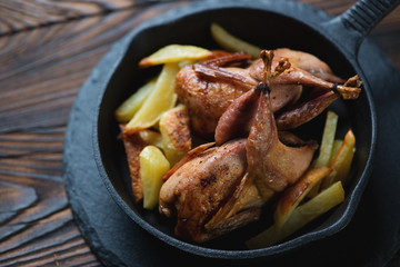 Baked quails with roasted potato in a cast-iron frying pan