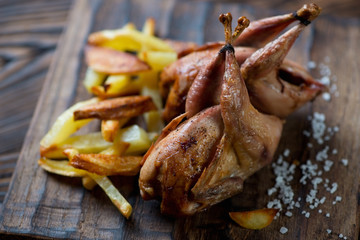 Close-up of whole roasted quails served with potato wedges