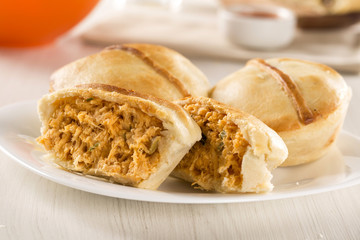 Empada Brazilian snack. pie with chicken on white plate on woode