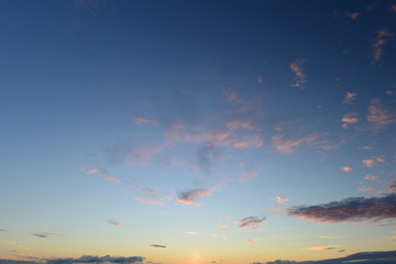 Azure blue sky above the sun leaving in clouds