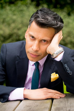 Frustrated businessman sitting at a table resting his head against his hand.