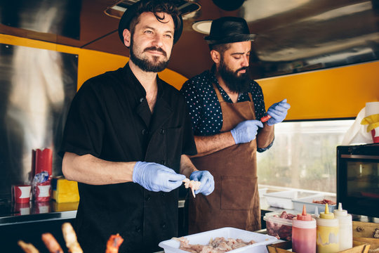 Pair of stylish male chefs prepares meat on wooden skewer