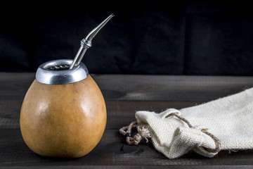 Yerba mate with bombilla and linen bag on wooden background