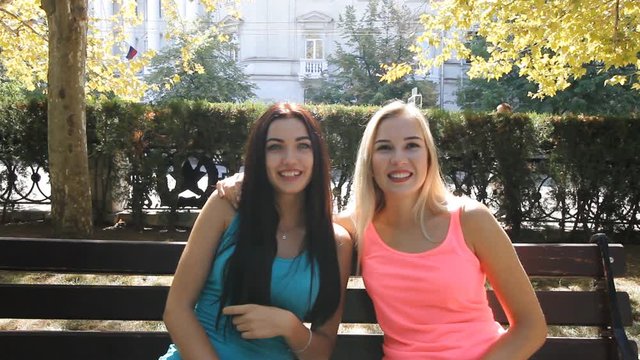 Two beautiful girls blonde and brunette girlfriend sitting in the park for a walk and spend time laughing fun