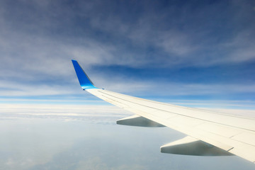 Wing of an airplane flying above the clouds on blue sky background
