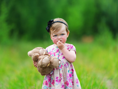Little girl standing in grass holding large teddy bear.