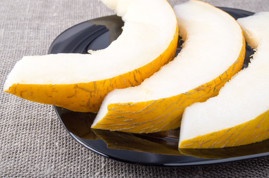 Pieces yellow melon on a black plate